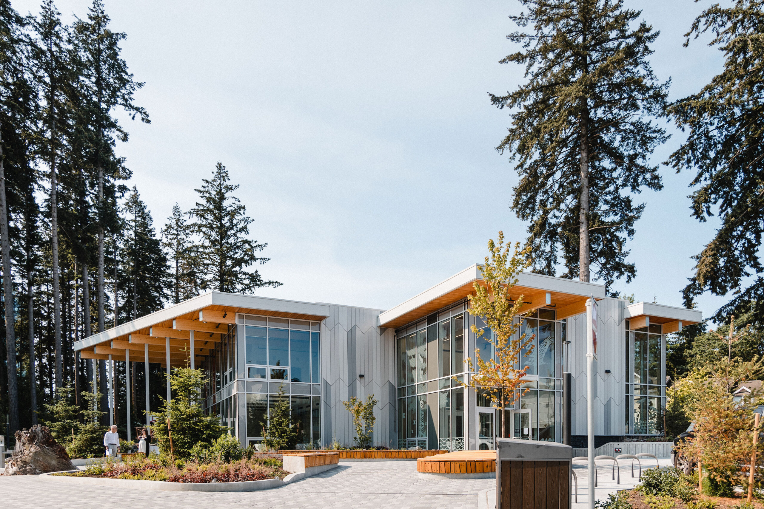 Exterior of lelษmฬ Community Centre at 5490 Shortcut Road, developed by Musqueam Capital Corporation within the University Endowment Lands, featuring a modern glass-and-wood design set within a forested landscape.