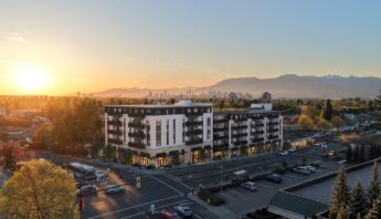 Abode mixed-use rental development at East 33rd Avenue and Victoria Drive at sunset, with the Vancouver skyline and North Shore mountains behind