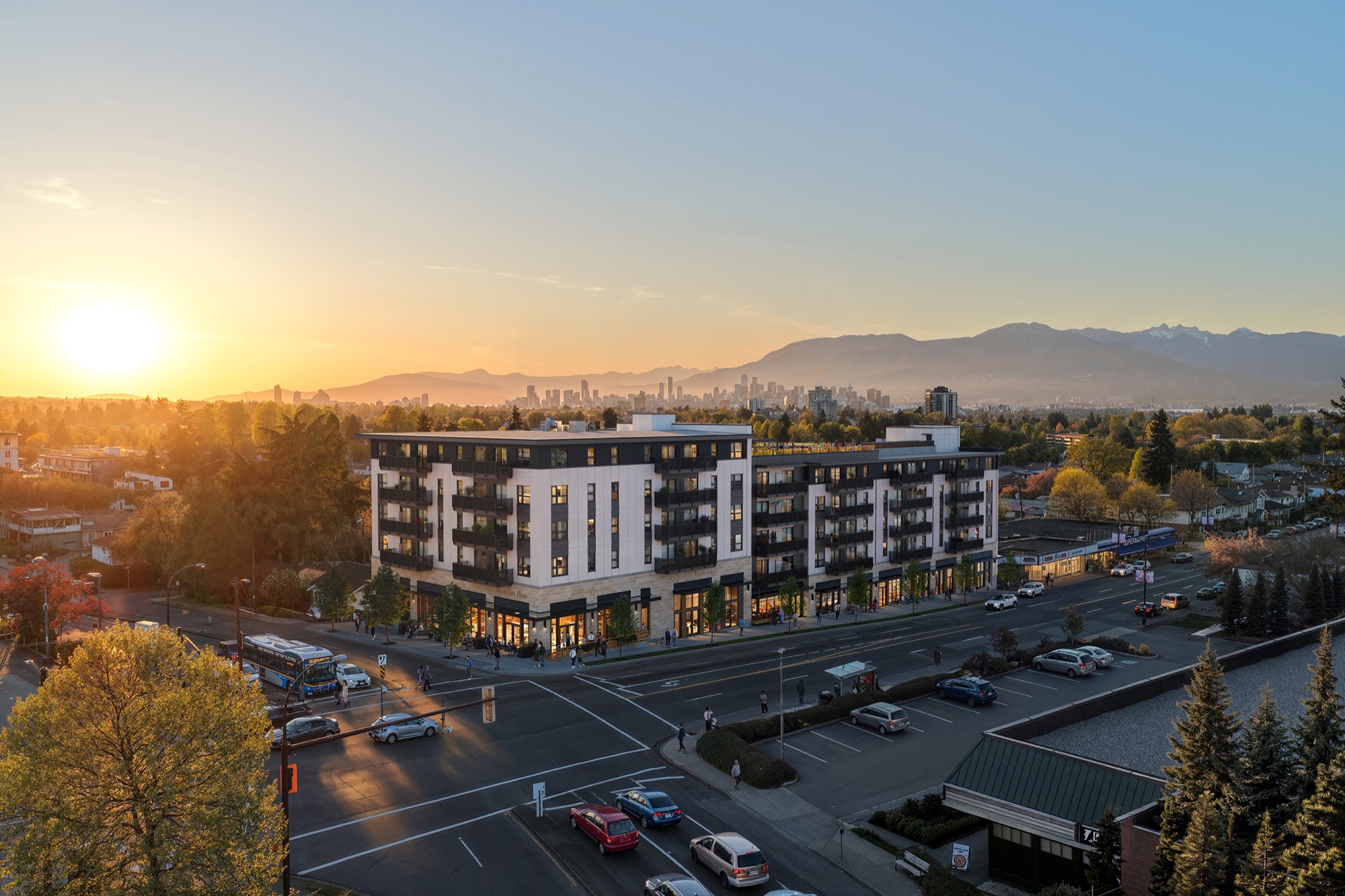 Abode - 4855 Victoria Drive Abode mixed-use rental development at East 33rd Avenue and Victoria Drive at sunset, with the Vancouver skyline and North Shore mountains behind