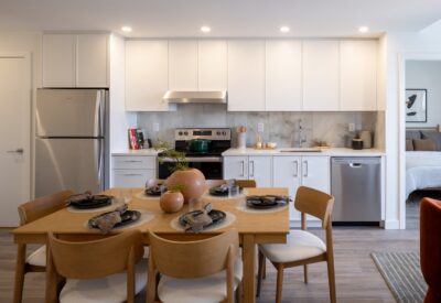 Open kitchen with white cabinetry, stainless appliances and a wood dining table in an Abode rental home